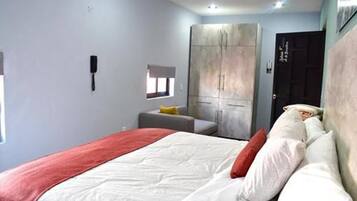 Un dormitorio con cama, armario, mesita y ventana.