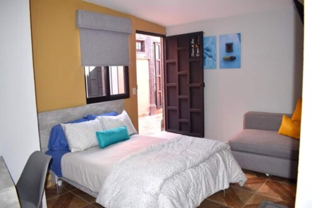 Un dormitorio con una cama, un sofá gris, una ventana y una puerta.