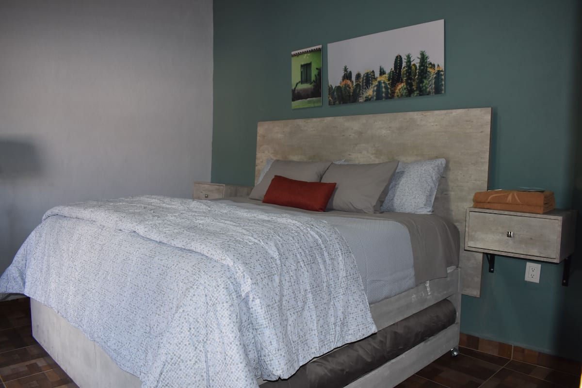 Un dormitorio con cama, mesitas de noche, un aparador y dos cuadros colgados en la pared.