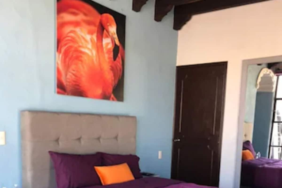 A bedroom with a bed, a nightstand, a mirror, and a door.