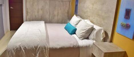 Un dormitorio con cama, cabecera de madera, mesita de noche y una silla.