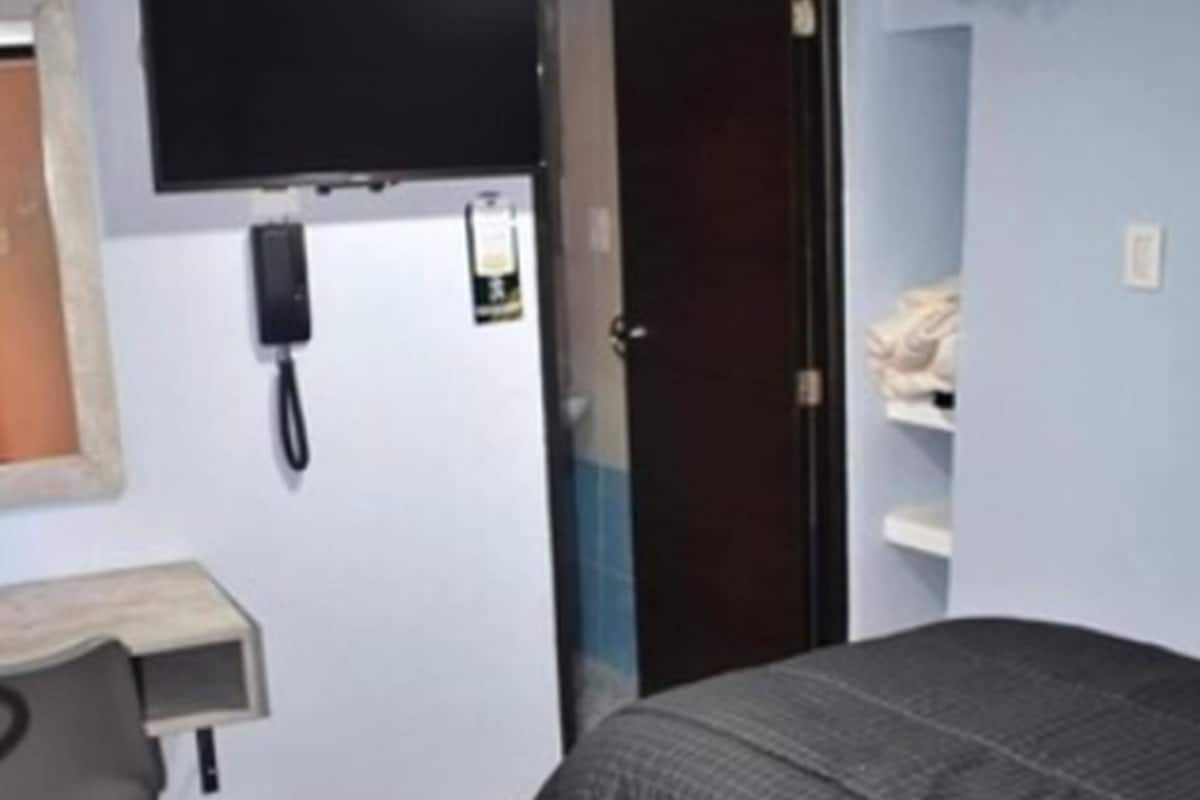 Un dormitorio con una cama, un escritorio con una silla, un teléfono y una puerta.
