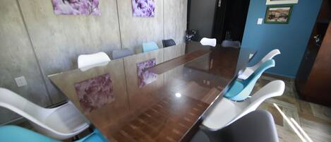 Un salón de conferencias con una mesa de vidrio, sillas blancas y azules, y un cuadro de flores en la pared.