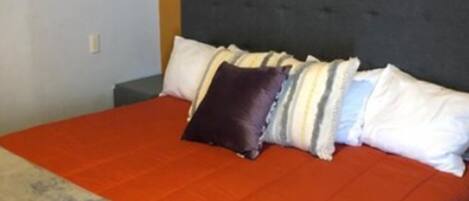 A bedroom with a large bed, a grey headboard, and a purple floral artwork on the wall.