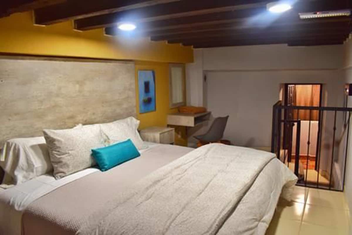 Un dormitorio con cama, escritorio y silla. Hay una ventana con cortinas y una puerta que da a un espacio exterior.