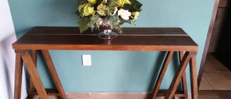 Uma mesa de madeira com um vaso de flores em frente a uma parede azul-esverdeada.
