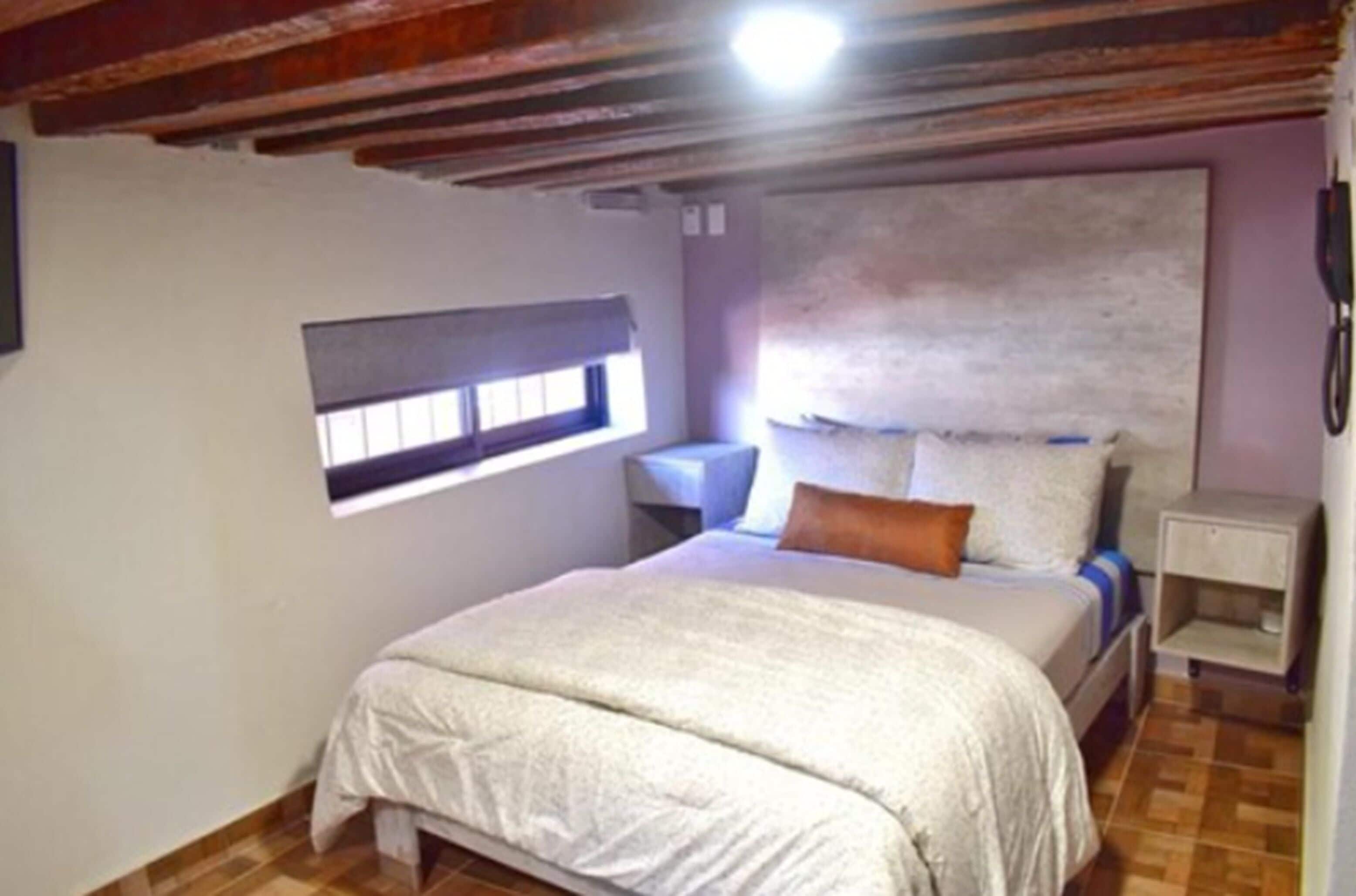 A bedroom with a bed, a nightstand, a window, and a wall-mounted telephone.