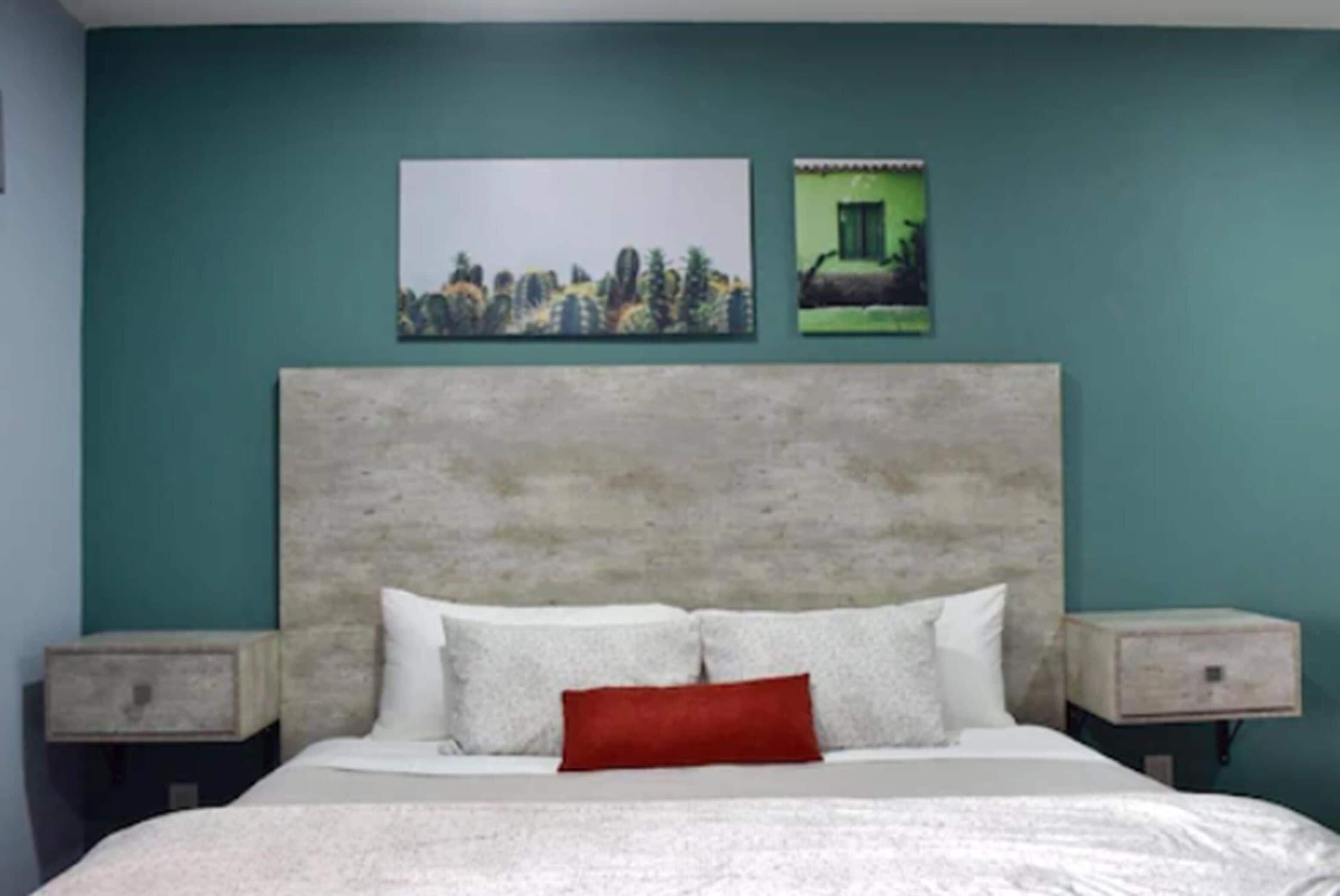 A bedroom with a large bed, two nightstands, and two wall-mounted paintings.