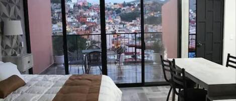 Una habitación de hotel con un balcón amplio, una cama, una mesa de comedor y sillas.