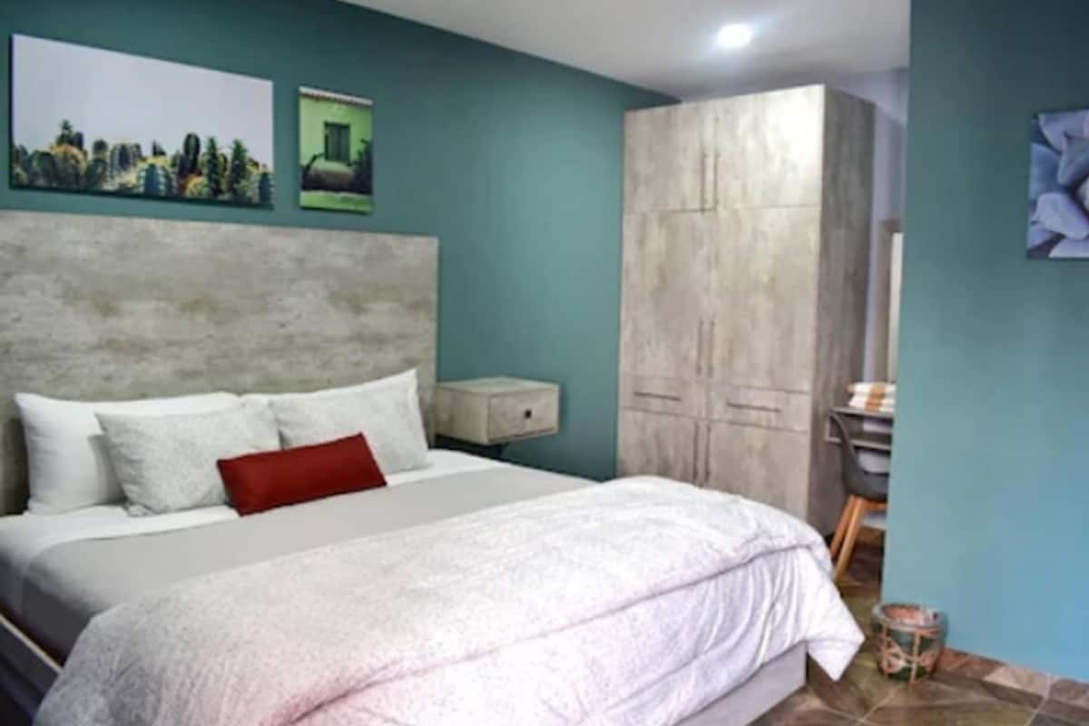 A bedroom with a bed, a wardrobe, a nightstand, and artwork on the walls.