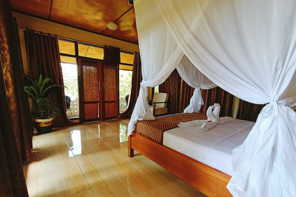 A room with a bed, curtains, a potted plant, and a view through a window.