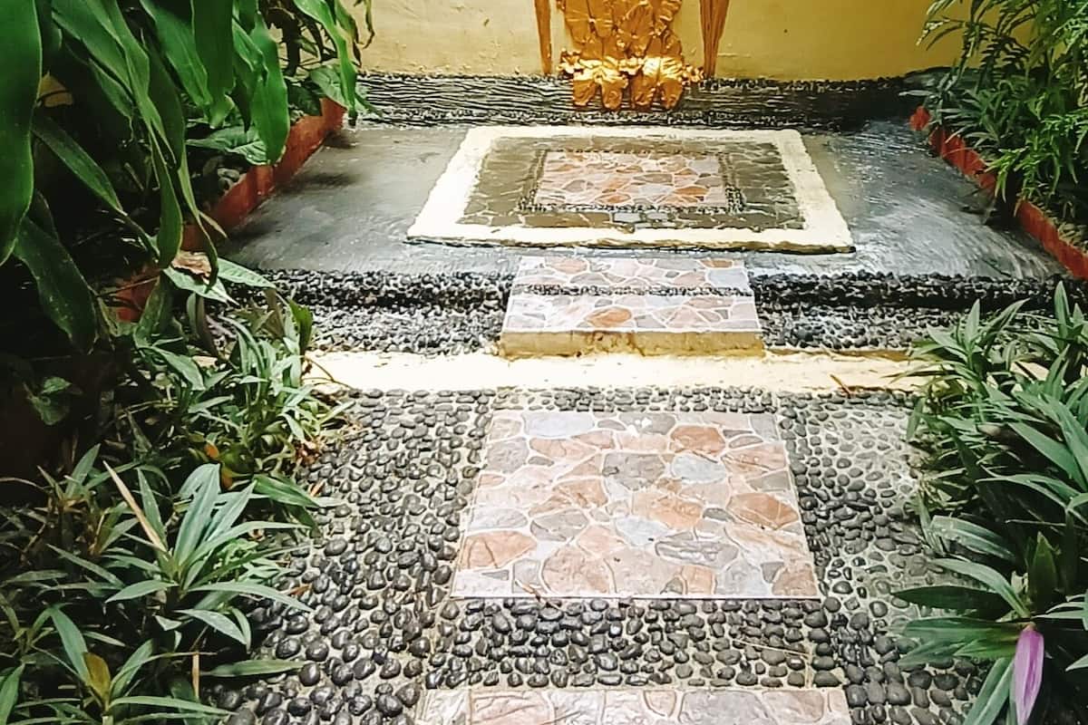 A stone pathway leading to a decorative golden statue, surrounded by lush greenery and a yellow wall.