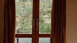 A view through a wooden-framed window with curtains, revealing a garden with various plants and a small pond. - Tangkoko Sanctuary Villa & Spa (Bitung)