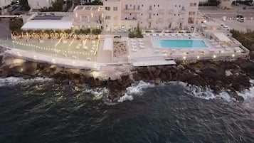 Un hotel sulla costa con piscina, posti a sedere all'aperto e un litorale roccioso.