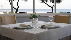 Mesa dispuesta para dos con vistas al mar, una planta en maceta y una ventana que da a la playa.