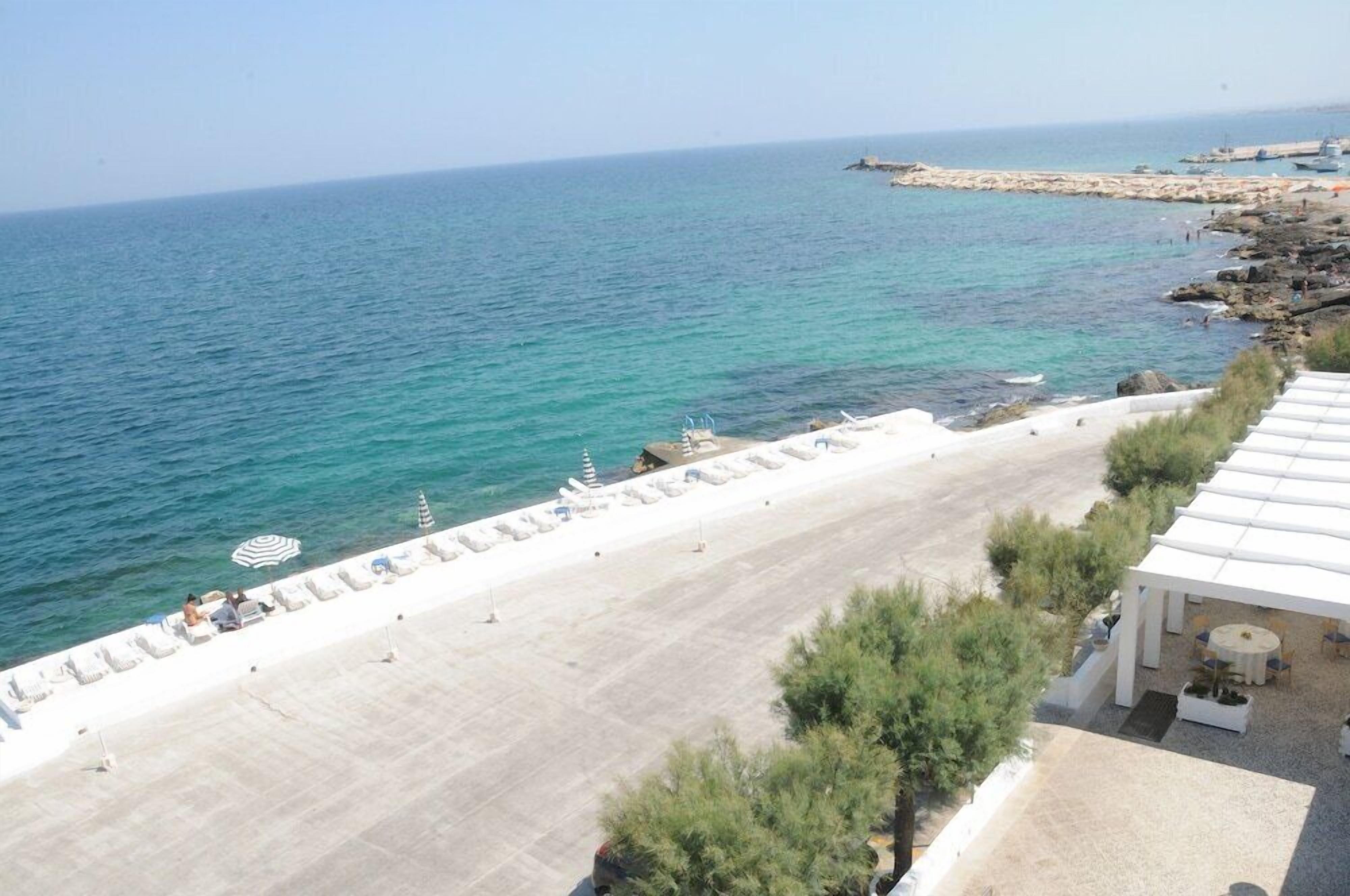 Una spiaggia con lettini e ombrelloni, una costa rocciosa e una vista limpida sul mare.