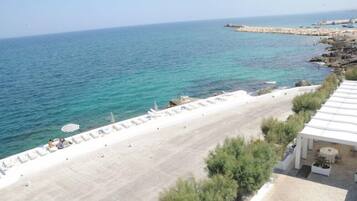 Una spiaggia con lettini e ombrelloni, una costa rocciosa e una vista limpida sul mare.
