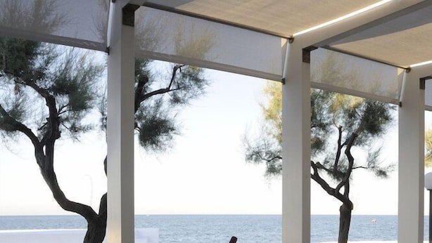 Mesa para dos con vista al mar, sillas de mimbre blanco y mantel blanco.