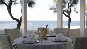 Un tavolo apparecchiato per due con vista mare, sedie in vimini bianco e tovaglia bianca.