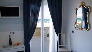 Una habitación con un escritorio blanco, una silla, un espejo y vistas a la playa a través de una puerta corrediza de vidrio.