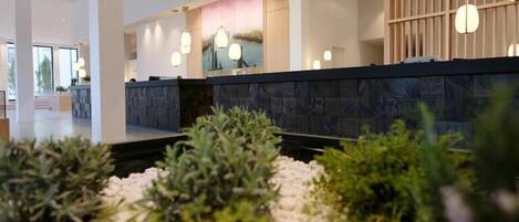 A modern hotel lobby with a reception desk, seating area, and a decorative wall with plants.
