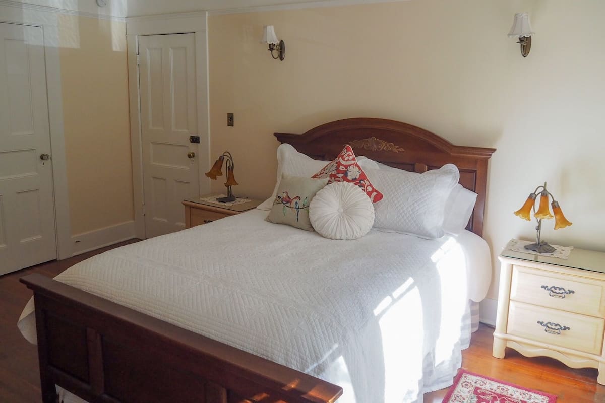 A bedroom with a wooden bed, white bedding, two bedside tables with lamps, a nightstand, and a door.