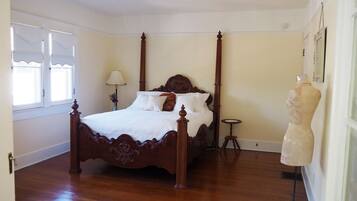 A four-poster bed with a wooden headboard, a bedside table, and a mannequin.