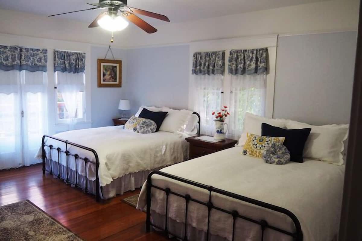 A bedroom with two beds, a ceiling fan, and a nightstand with a lamp.