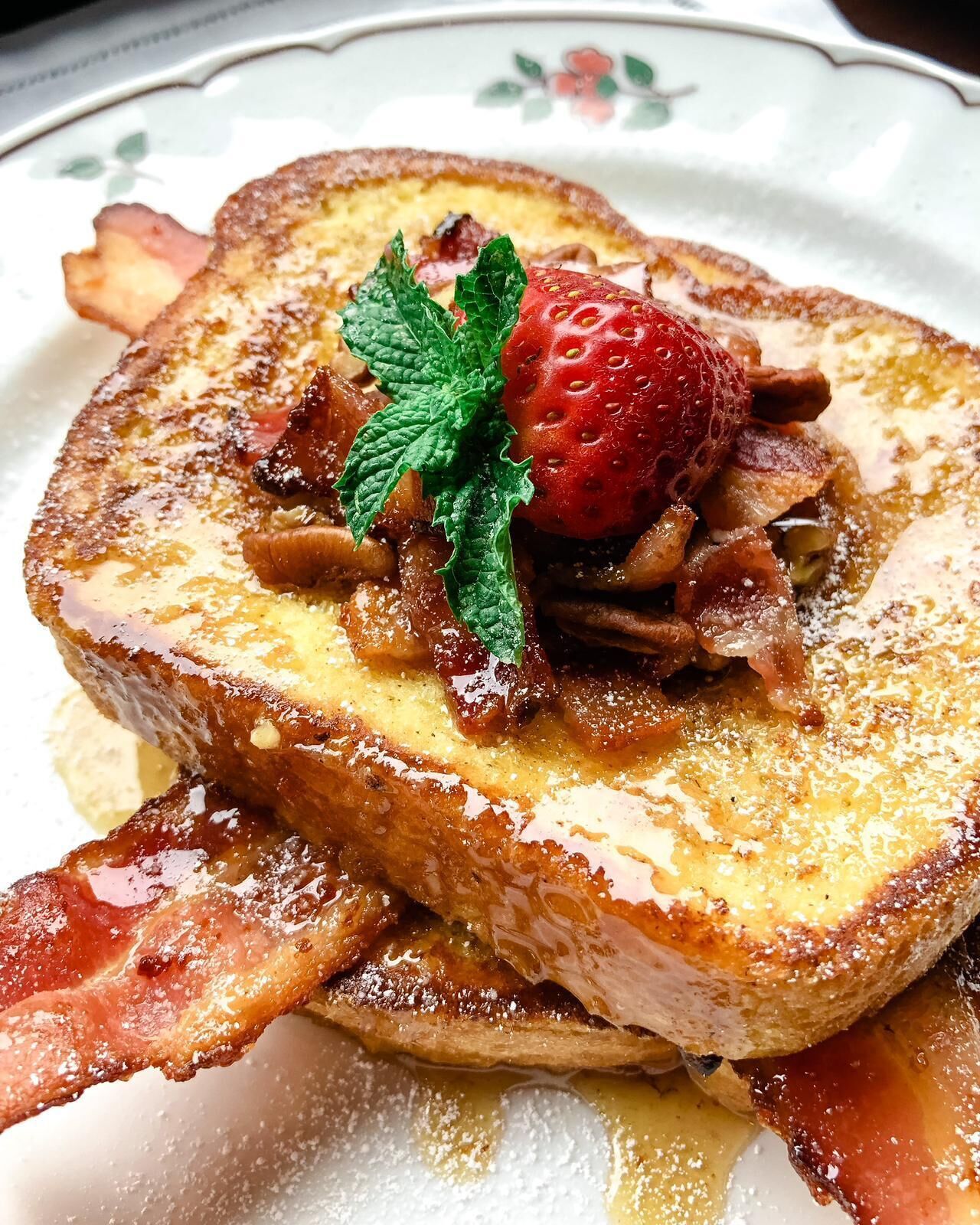 Een bord met French toast, aardbeien, munt en bacon.