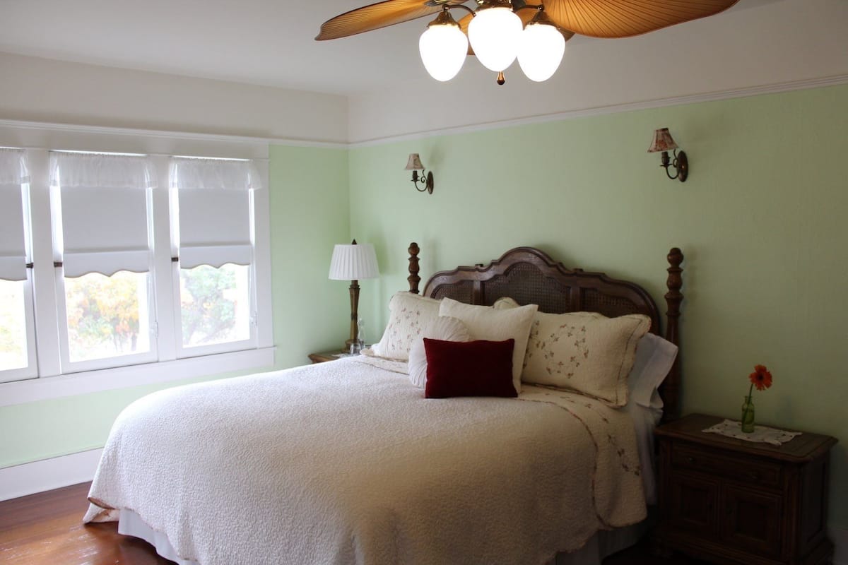 A bedroom with a bed, a nightstand, a lamp, and a window with curtains.