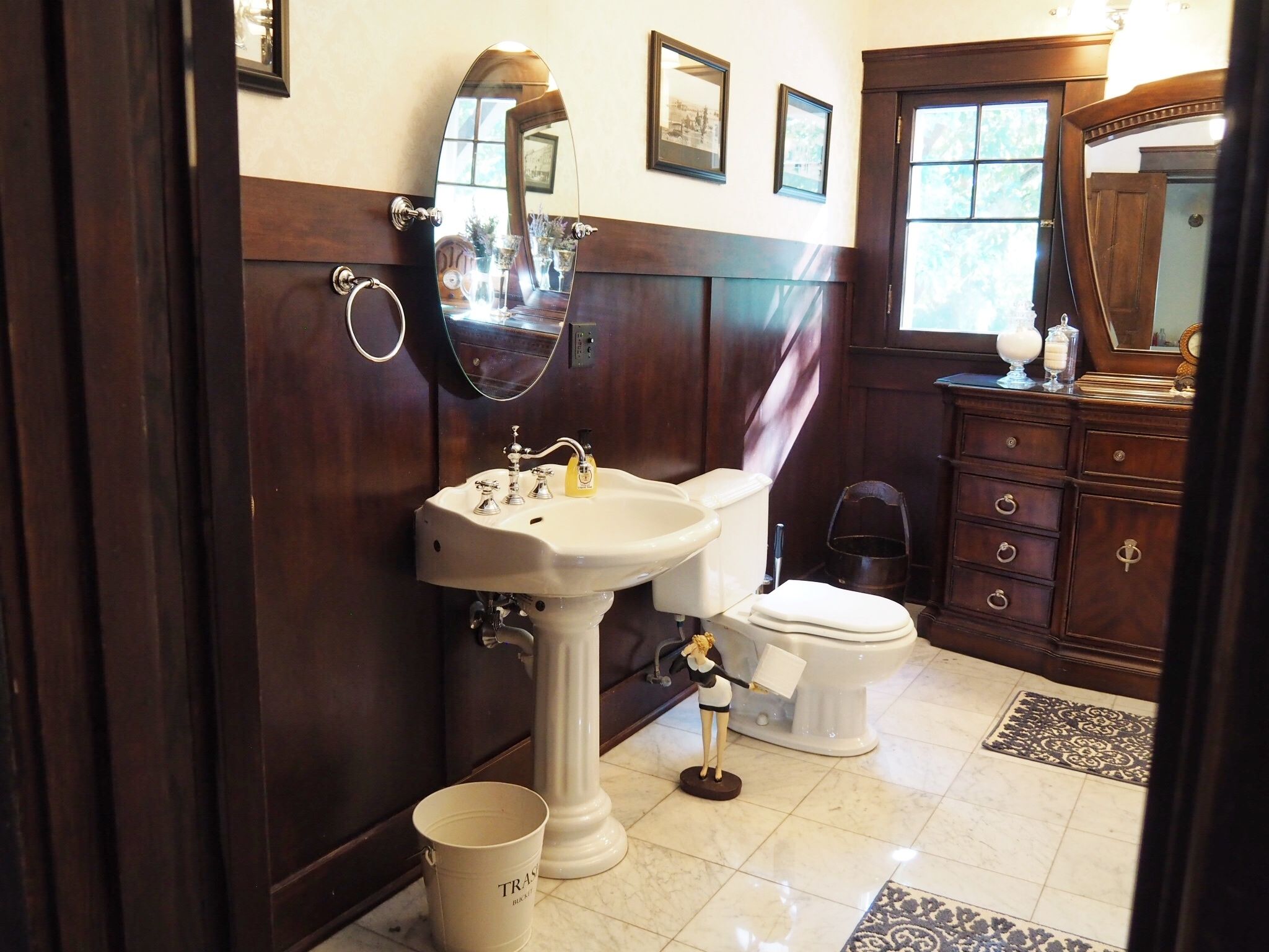 A bathroom with a pedestal sink, toilet, and a wooden vanity with drawers.