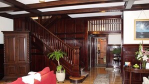 Un amplio salón con escalera de madera, un sofá rojo, una planta en maceta y una mesa con un jarrón.