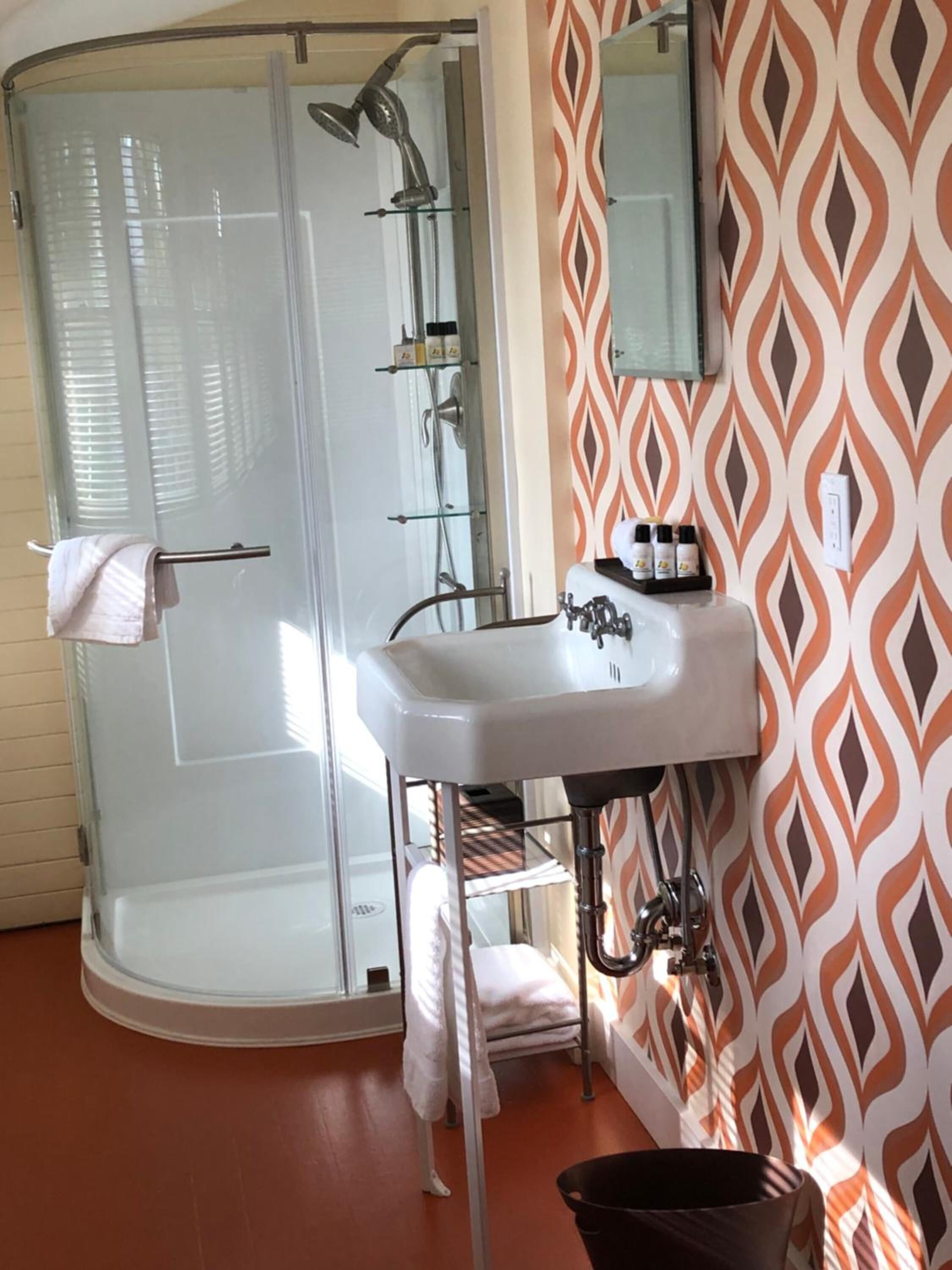 A bathroom with a glass shower enclosure, a white sink, and a patterned wall.