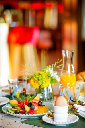 A breakfast setting with a plate of fruit, a glass of orange juice, and a vase of flowers.