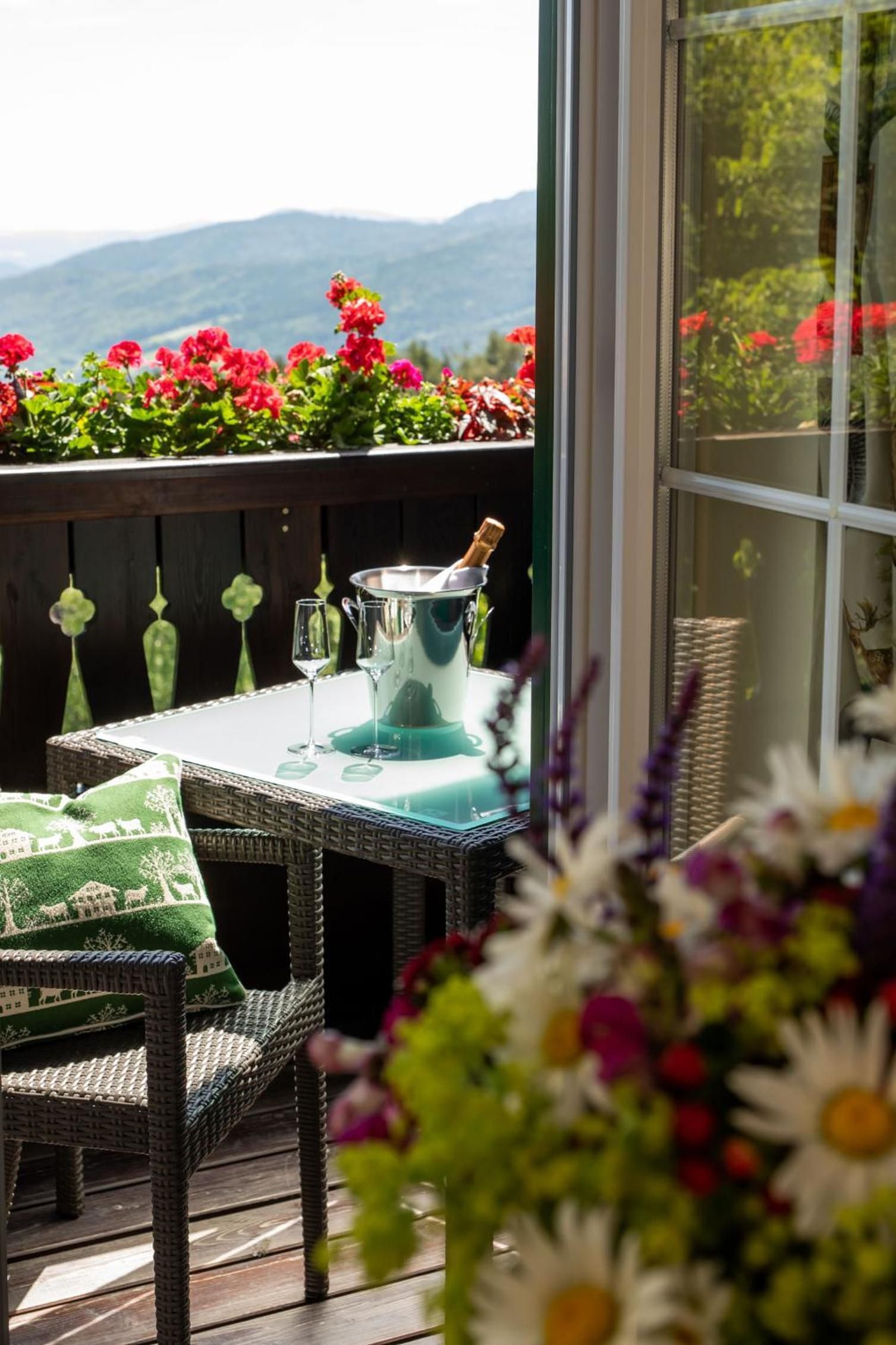 A patio with a table set for two, a champagne bottle, and a view of mountains.