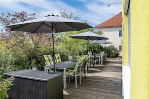 Un patio al aire libre con mesas, sillas, sombrillas y una terraza de madera.