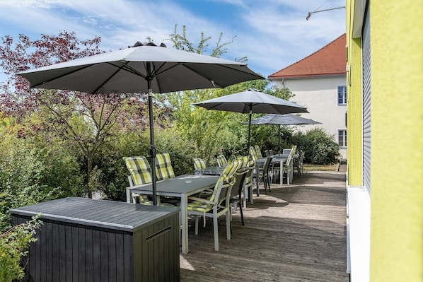 An outdoor patio with tables and chairs, umbrellas, and a wooden deck.