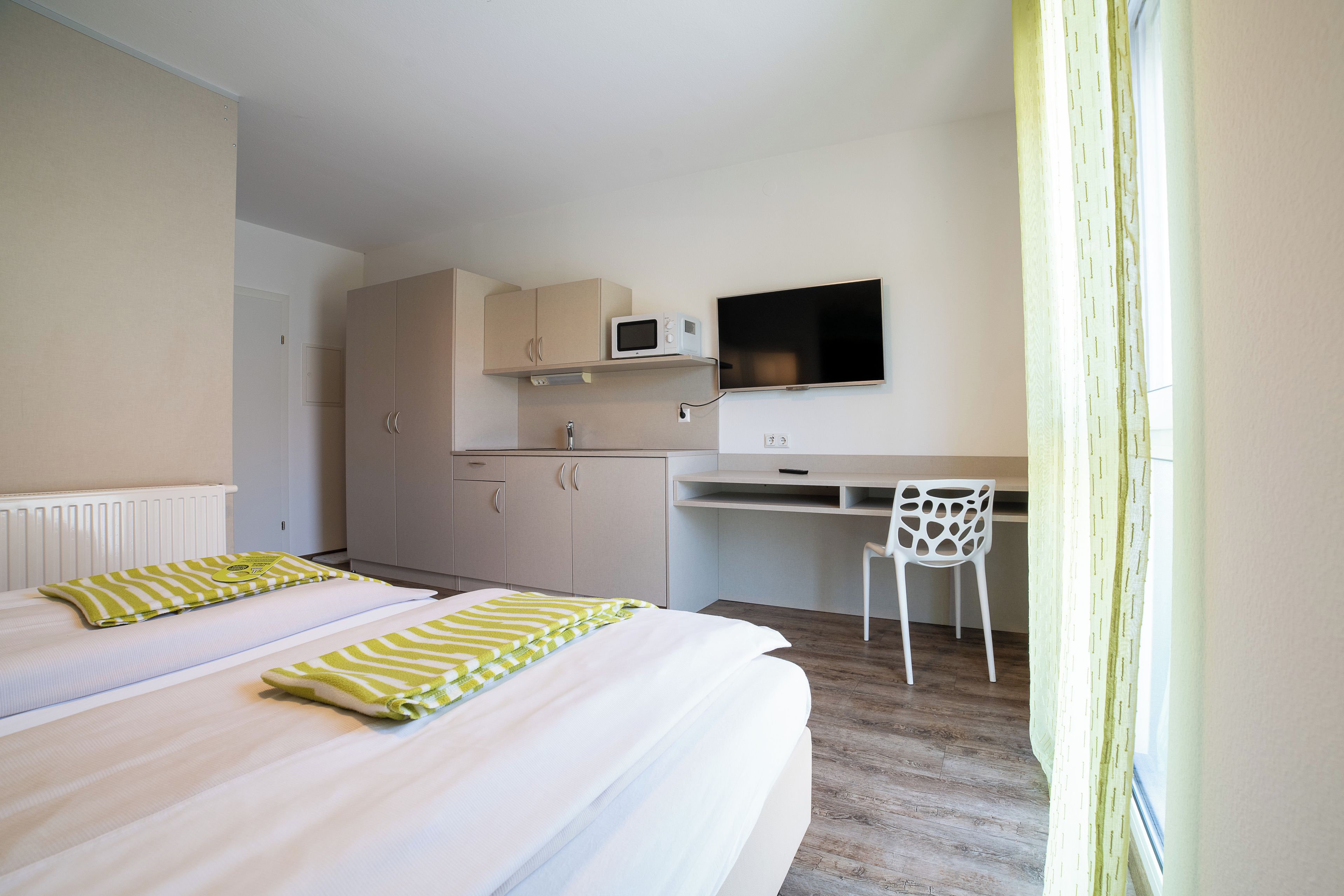 A hotel room with two beds, a desk, a chair, a television, and a window with curtains.