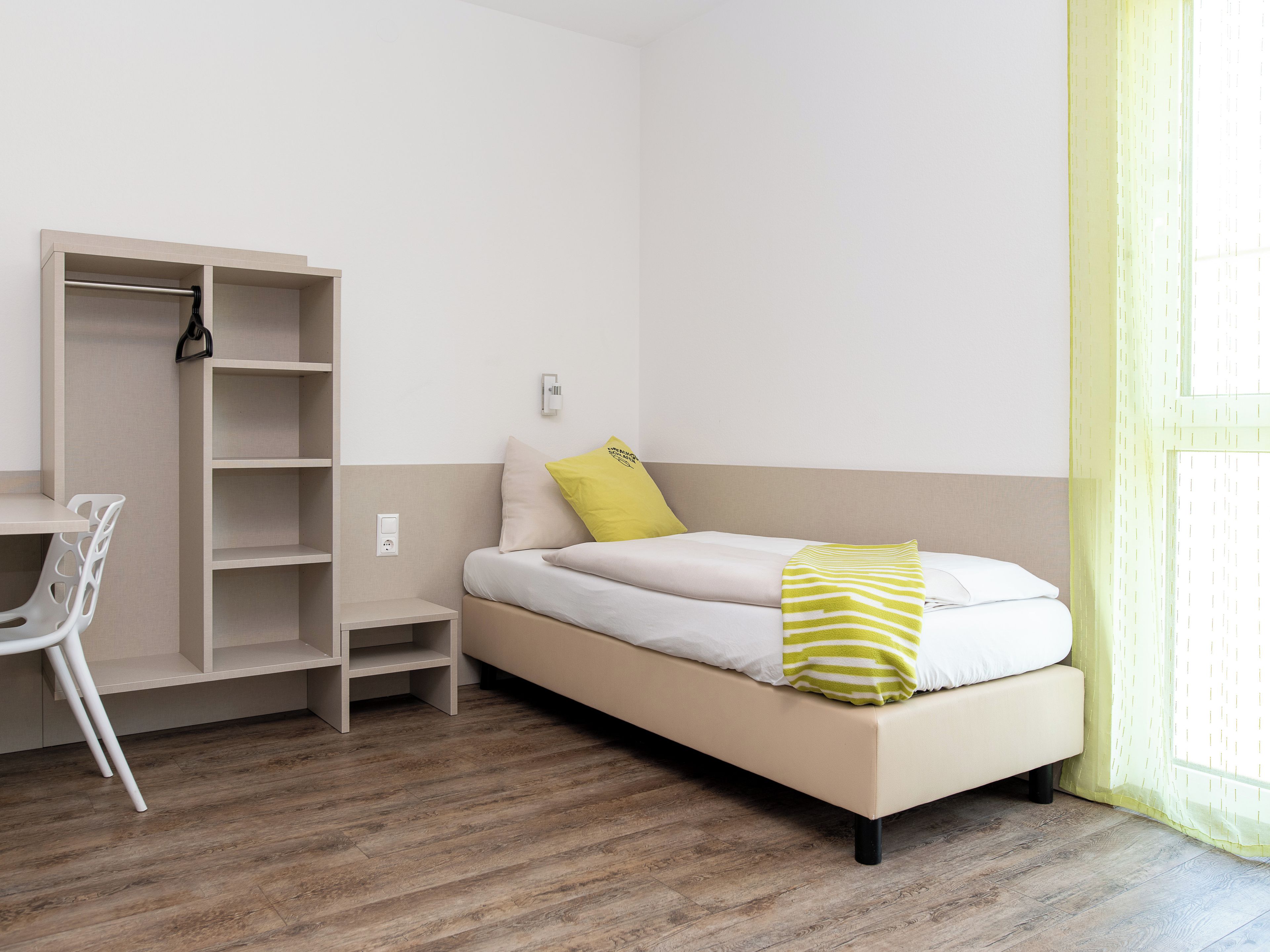A bedroom with a bed, a desk, and a wardrobe.