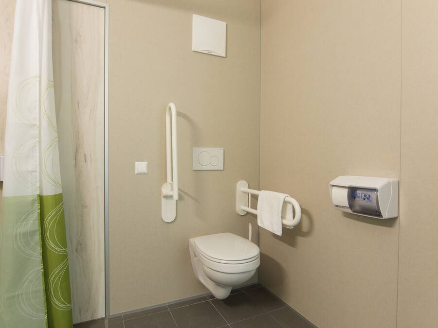 Un baño pequeño y privado con inodoro, barandilla, dispensador de toallas y cortina de ducha.