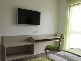 Habitación de hotel con cama, escritorio, silla, televisor y ventana con cortinas.