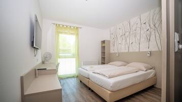 A bedroom with a bed, a TV, a radiator, a window with curtains, and a wall with a tree mural.