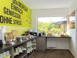 Un área de cocina con una pared amarillo brillante, una cafetera y una ventana con vistas a árboles.