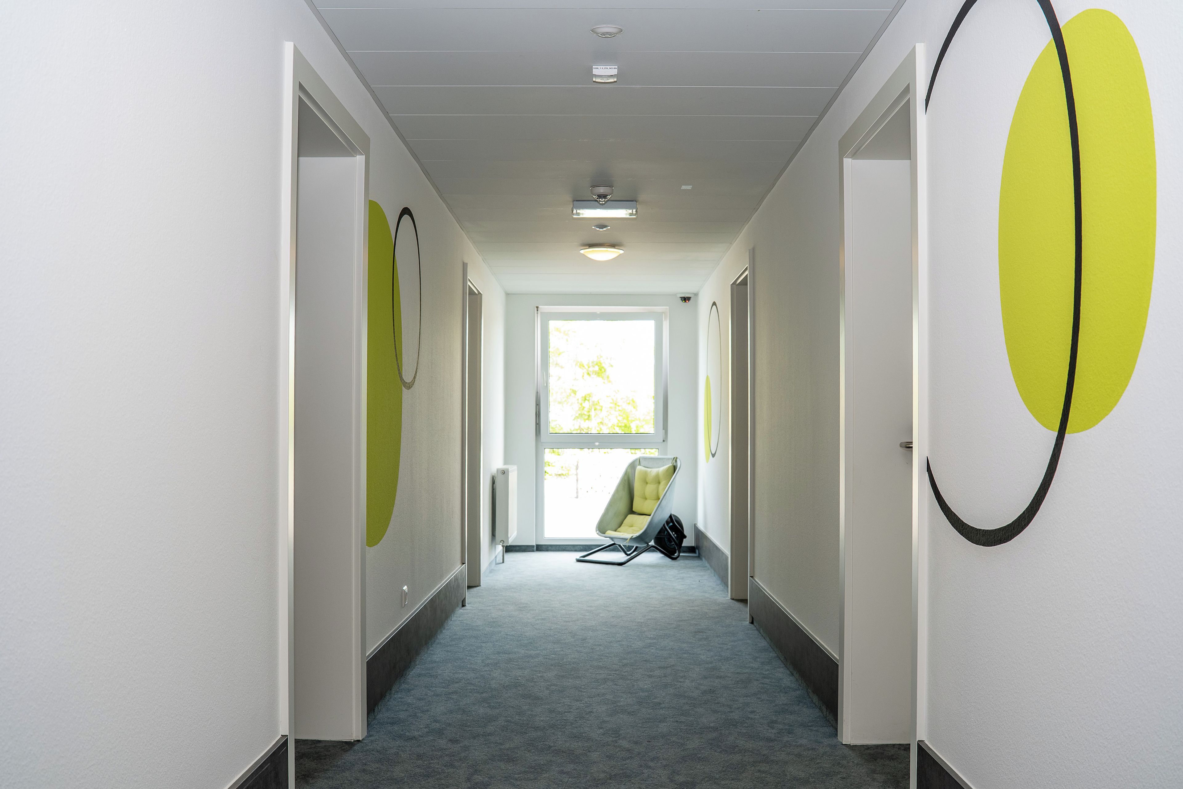 En hall med en stol och en väska, som leder in till ett ljust rum med ett fönster.