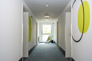 A hallway with a chair and a bag, leading to a bright room with a window.