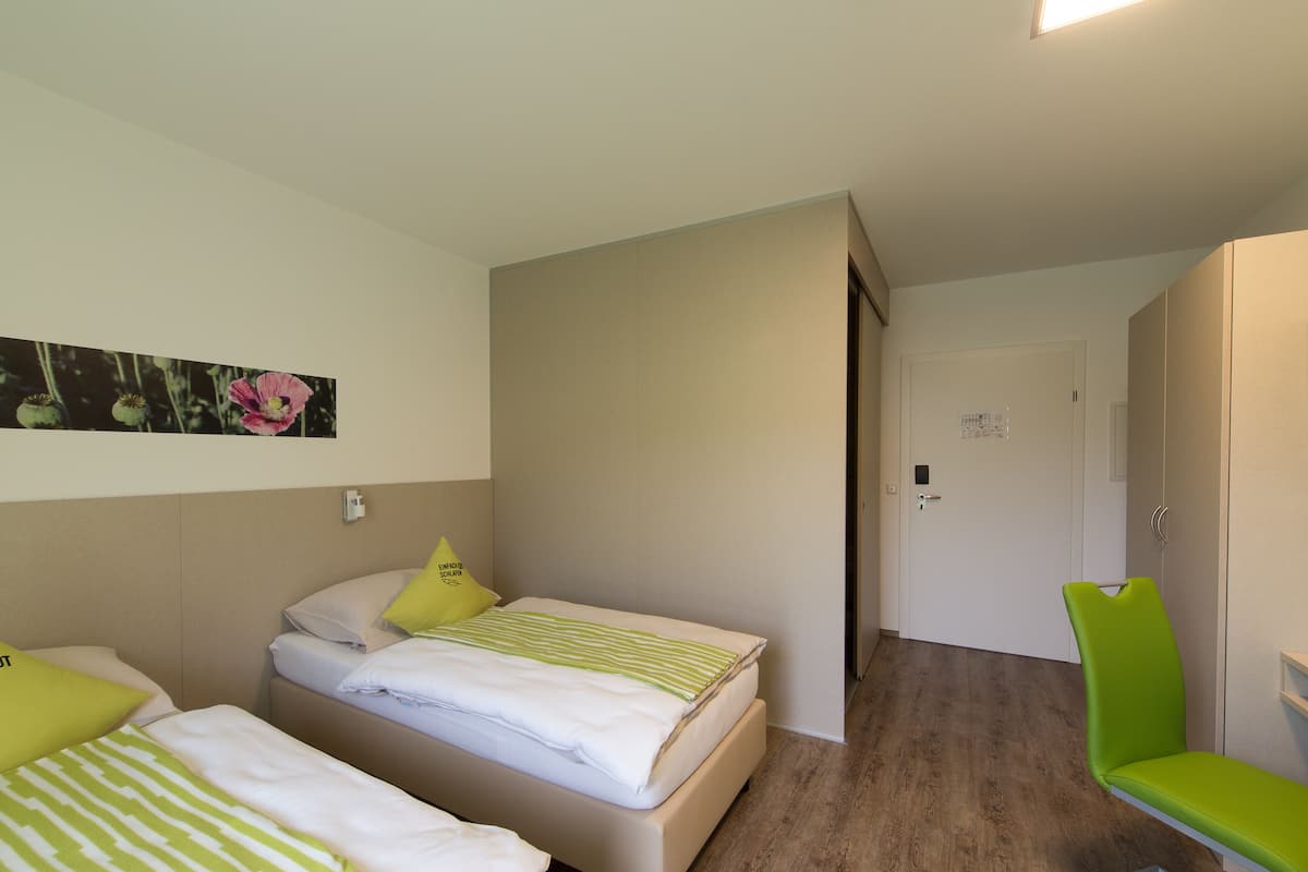Habitación de hotel con dos camas, una silla verde y suelo de madera.