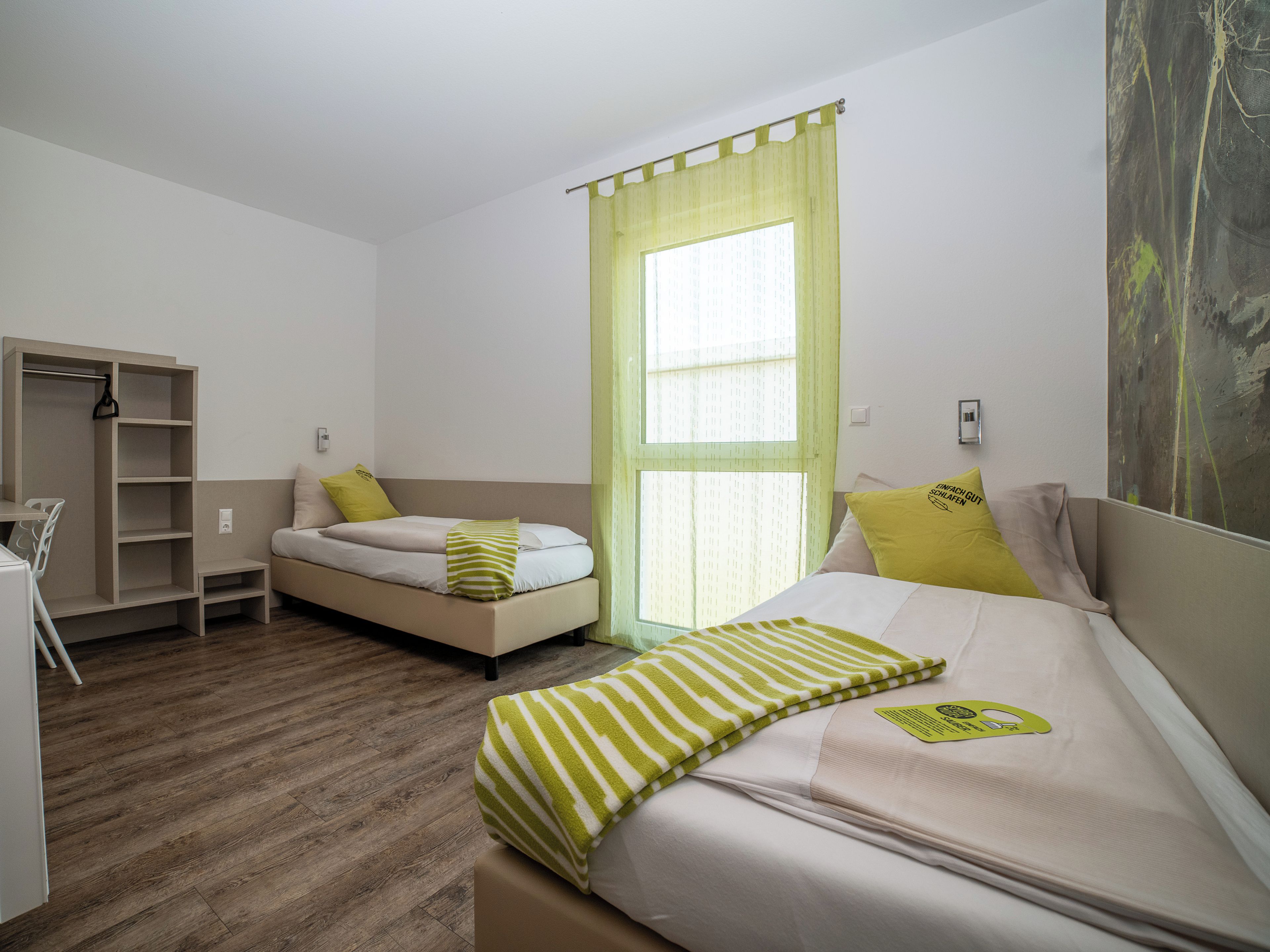 Ein Schlafzimmer mit Bett, Schreibtisch, Stuhl, Kleiderschrank und einem Fenster mit Vorhang.