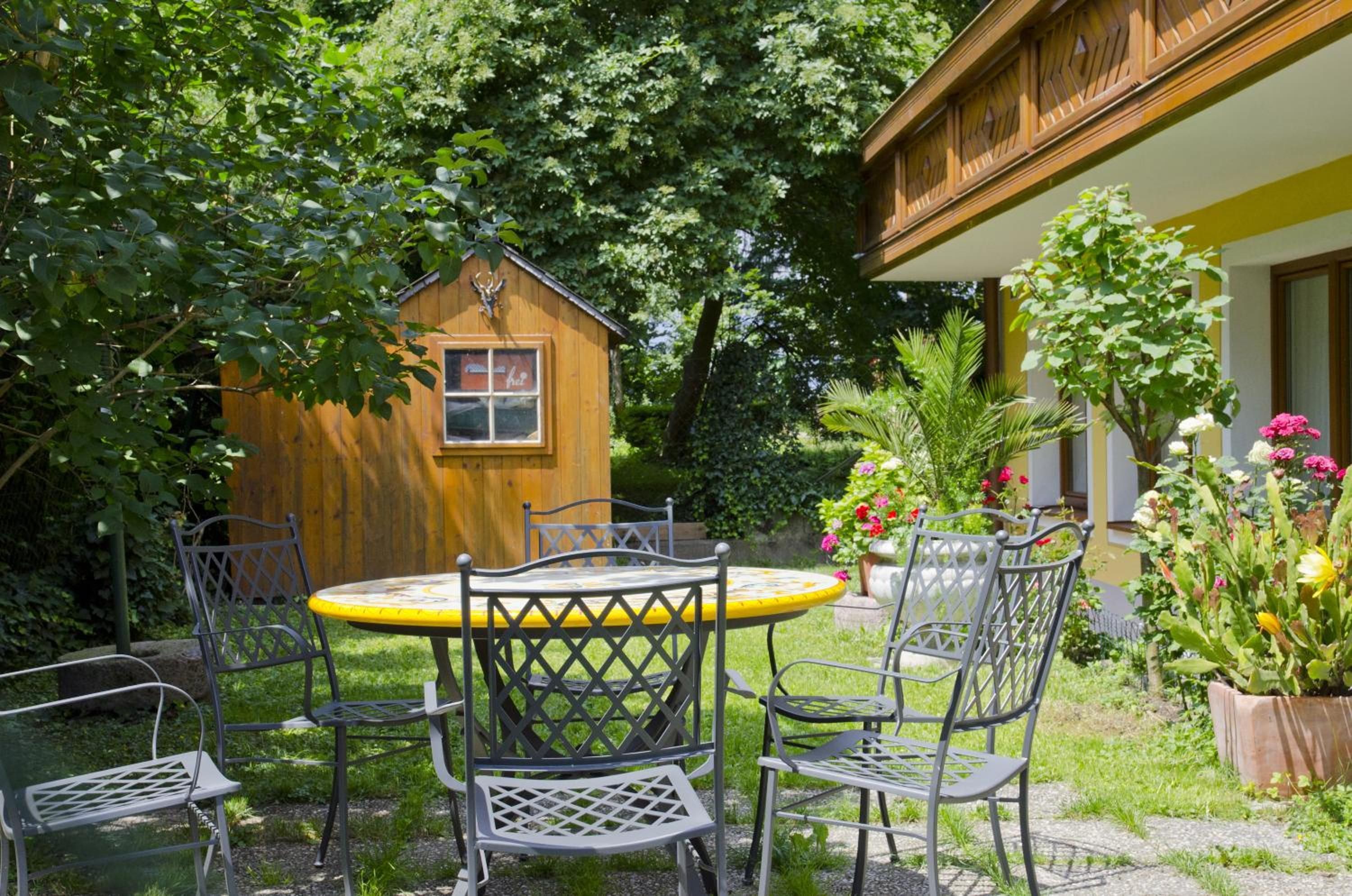 A wooden cabin with a window, surrounded by lush greenery and a garden with various plants and flowers.