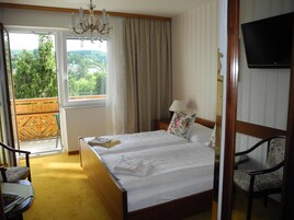 Habitación de hotel con cama, televisión, ventana con cortinas y vista a zonas verdes.