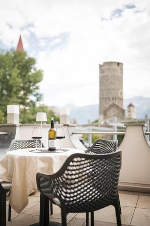 A table set outdoors with a bottle and glasses, overlooking a cityscape with a prominent tower.